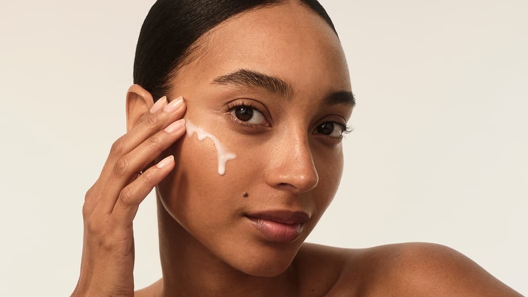 Eine Frau trägt eine Creme auf ihr Gesicht auf. Ihre Haut ist rein und glowy.