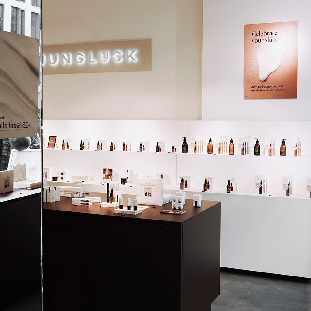 Ein Einblick in den JUNGLÜCK Store mit Braunglasflaschen, Pflegeprodukten und einer Wandtafel mit dem Slogan 'Celebrate your