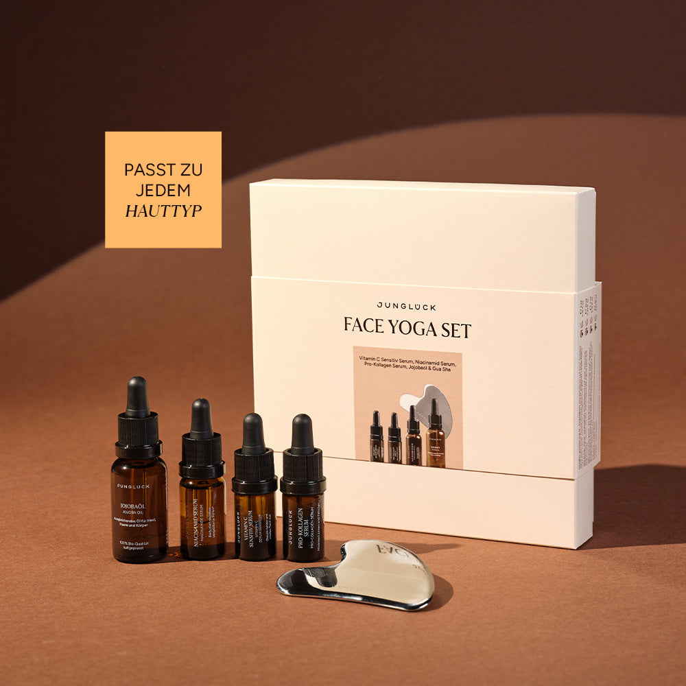 Facial oil bottle set with dropper and a silver facial massage tool beside sleek white JUNGLÜCK Face Yoga Set box on brown.