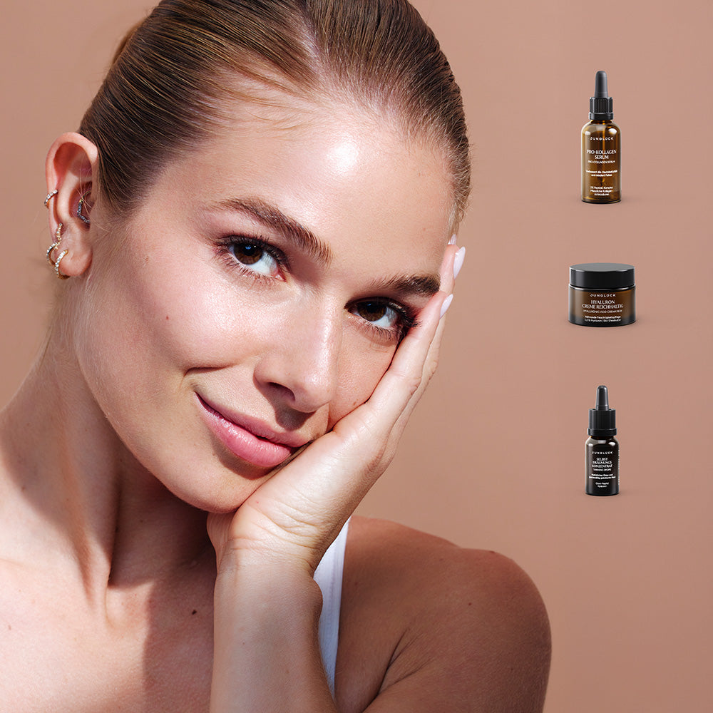 Woman with clear skin resting her face on hand alongside three skincare bottles with dropper caps and a jar on beige.