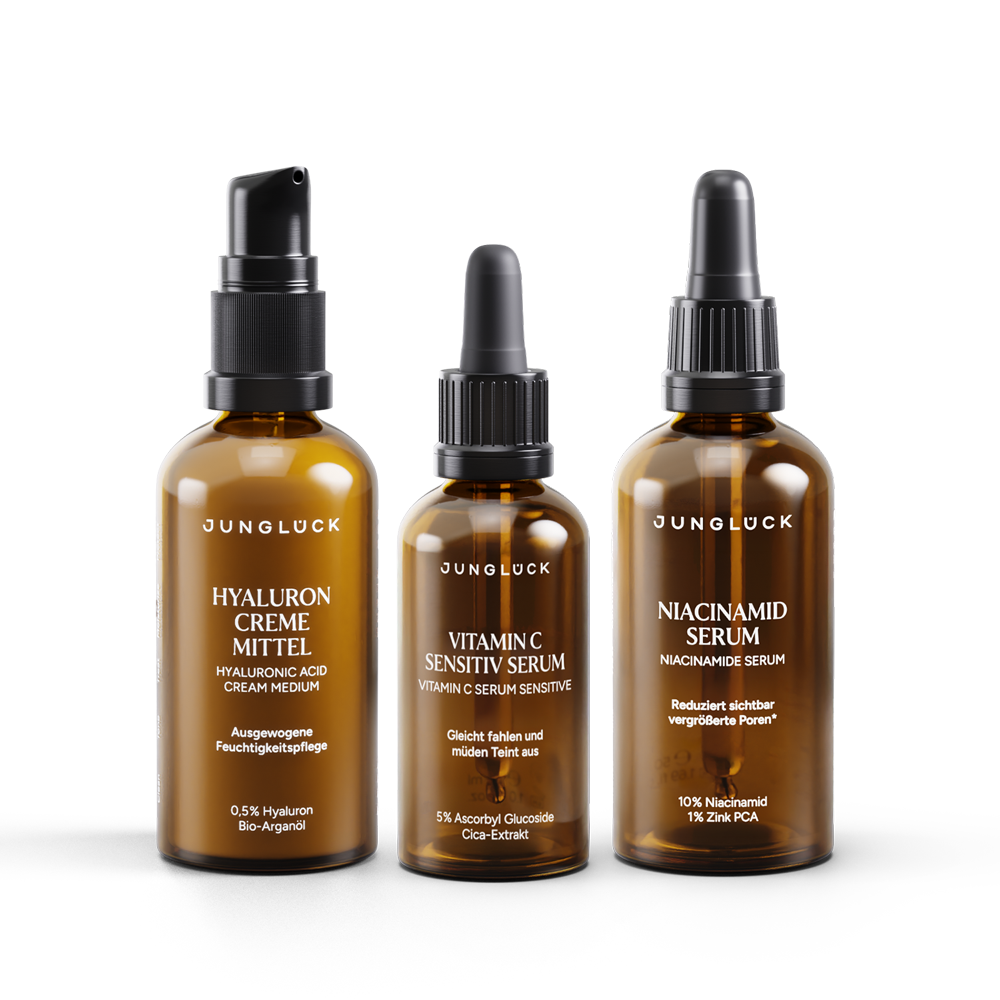 Three amber glass skincare bottles with black droppers and pump tops, labeled Hyaluron Creme Mittel, Vitamin C Expert Serum, .