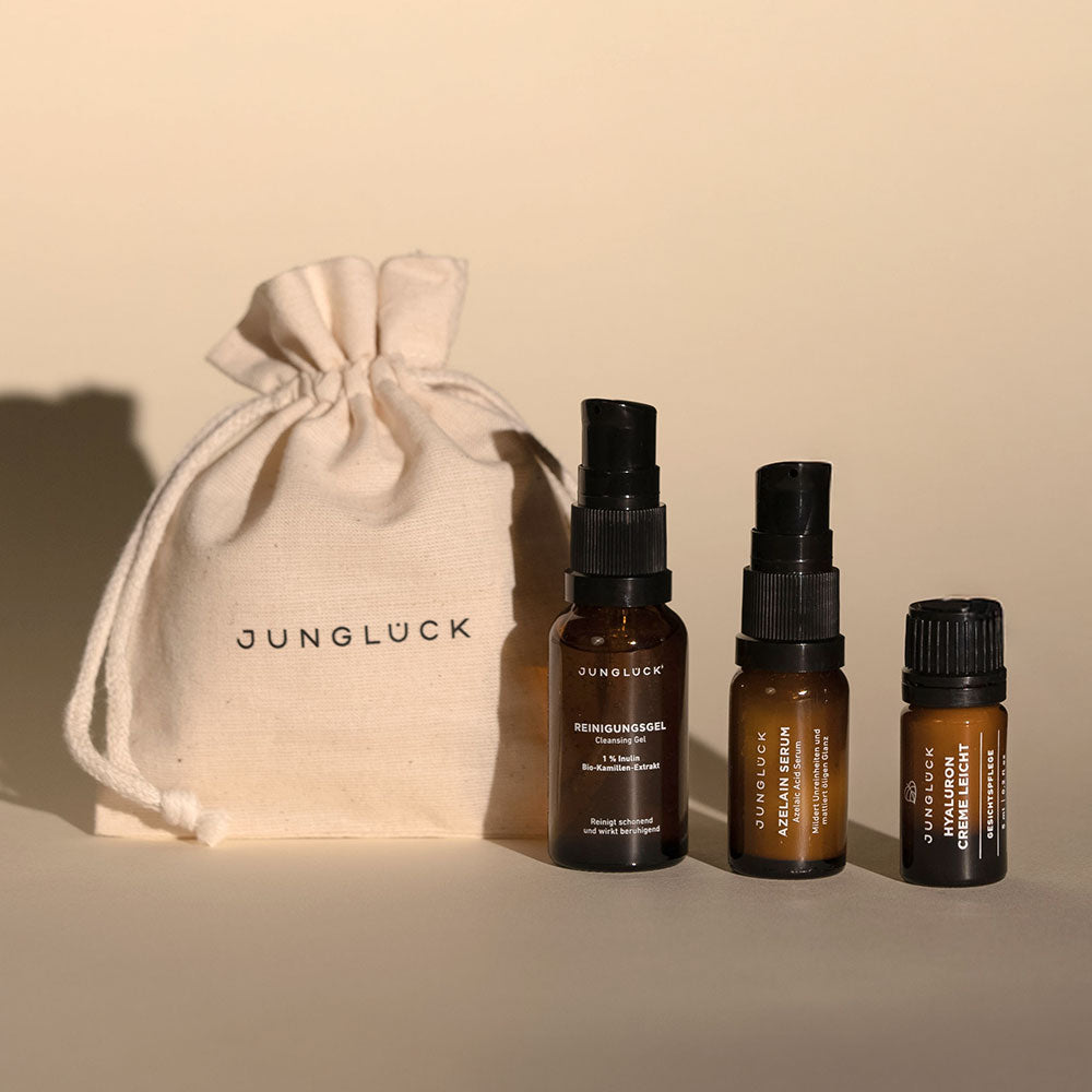 Three amber glass serum bottles with black pumps and caps next to a small beige drawstring pouch labeled Jungluck.