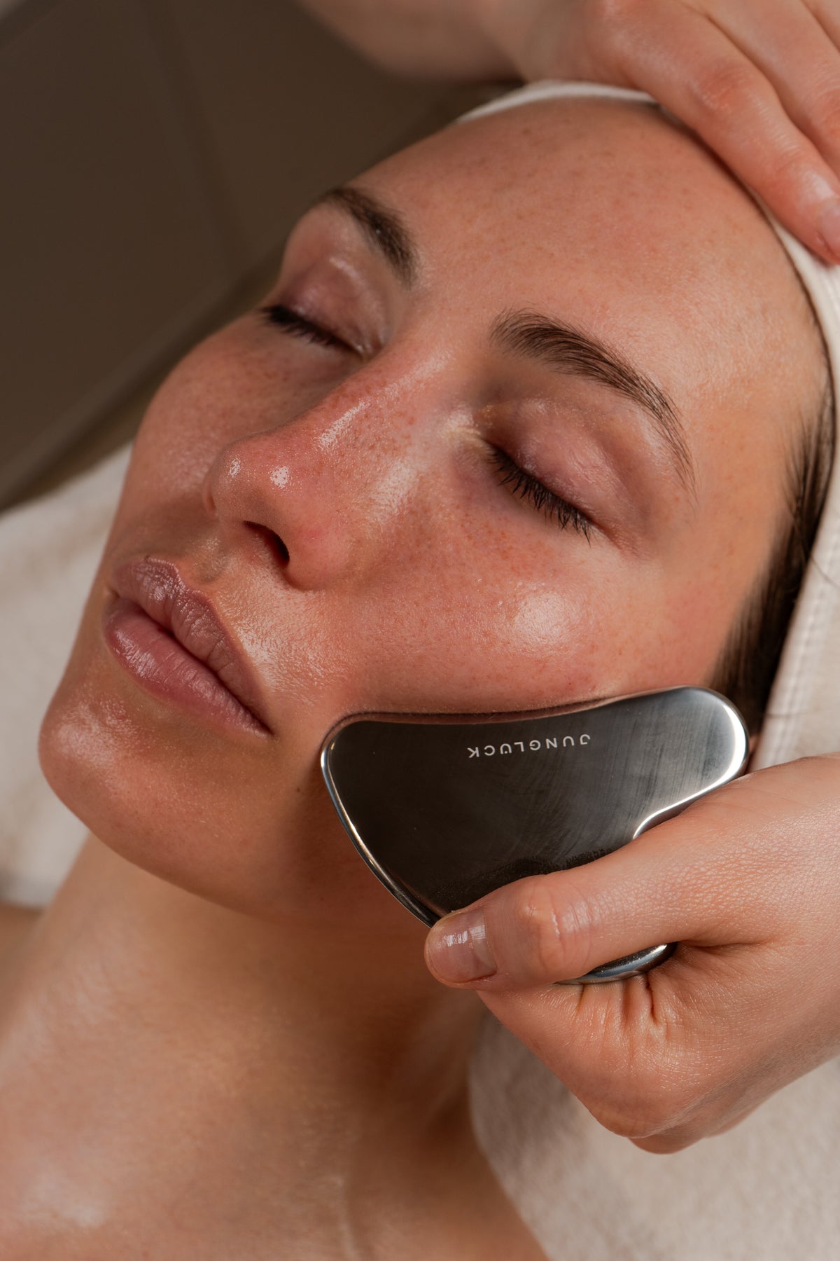 Eine Schönheitstherapeutin führt eine Gesichtsbehandlung mit einem Gua Sha Werkzeug durch. Die Frau entspannt mit